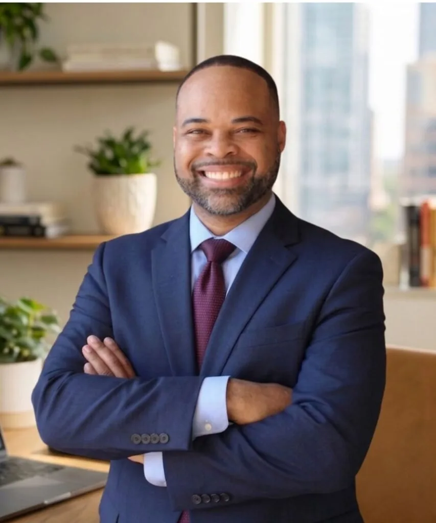 Monley Edmond in a navy suit, arms crossed, smiling.